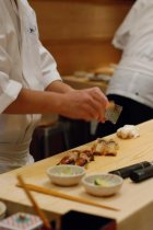 A chef's hands, preparing sushi with ingredients in small bowls