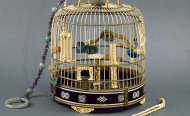 Gold birdcage with jade and amethyst string of beads coming from the top and fancy bird toys and perches inside.